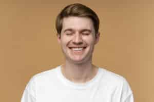 Young man smiling at camera wearing white shirt against tan background, professional headshot.