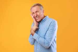 Middle-aged man in blue checkered shirt smiling against yellow background, dental professional portrait.