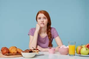 Woman with concerned expression at breakfast table surrounded by sugary foods and beverages.