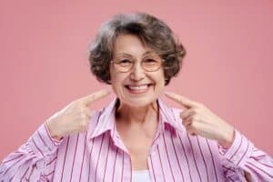 Smiling woman with glasses wearing striped purple shirt against pink background