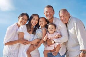 Multi-generational family smiling together outdoors against blue sky background.
