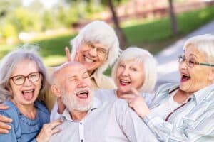 Four cheerful senior adults smiling outdoors in a park setting, displaying healthy teeth and dental health.