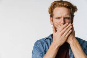 Man with hand over mouth experiencing bad breath or dental discomfort.