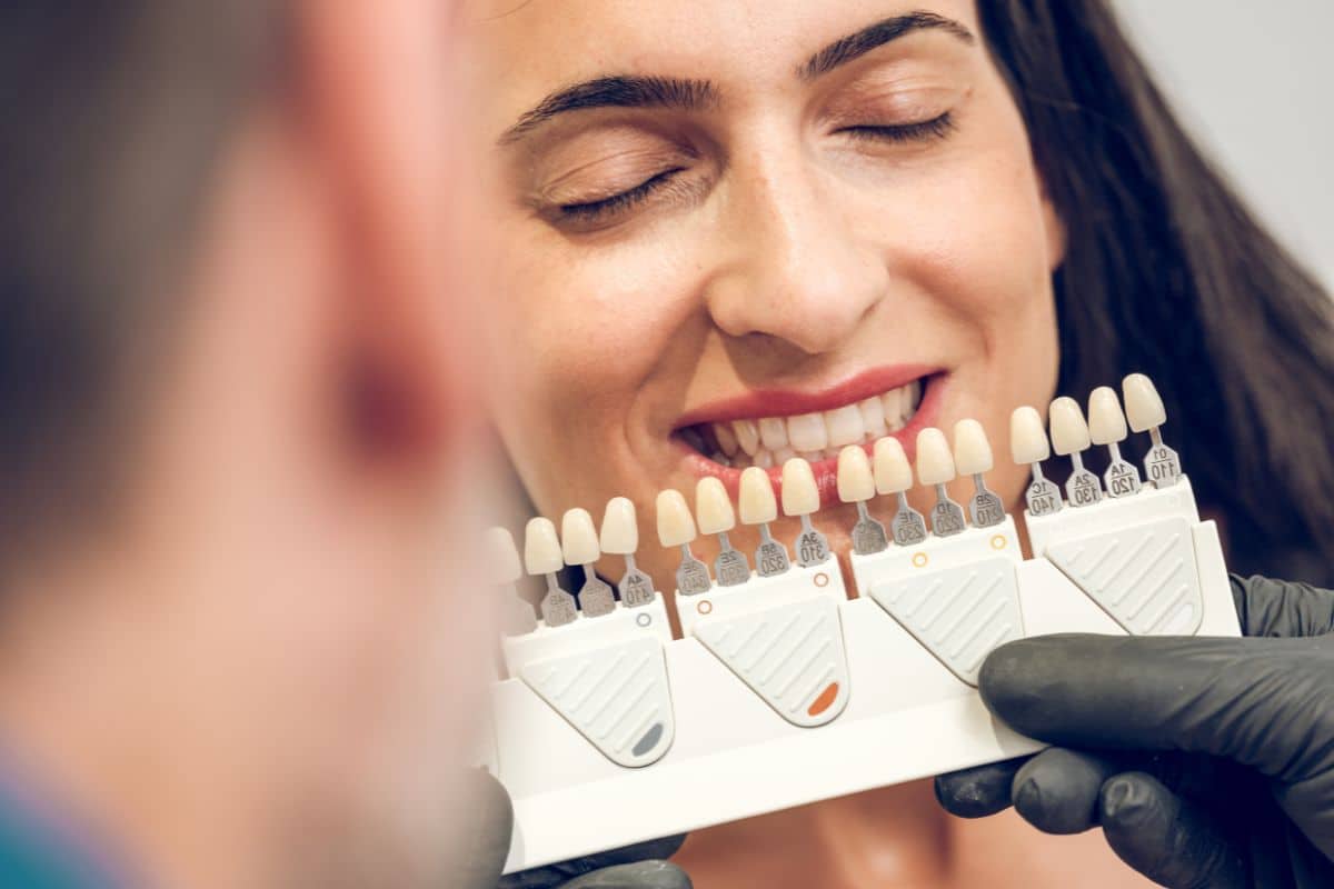 Patient comparing veneer shade samples during a cosmetic dentistry consultation to achieve a natural-looking smile.
