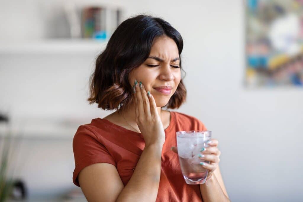 A woman reacts to discomfort while holding a cold drink, illustrating how sudden tooth sensitivity to cold foods and beverages may indicate enamel erosion, gum recession, or underlying dental issues.